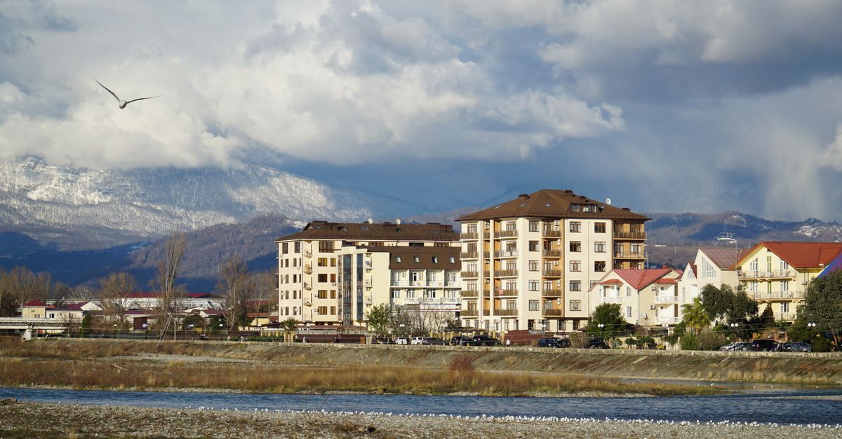Picturesque view of Adler town in Russia, showcasing buildings with a mountainous backdrop and cloudy sky.