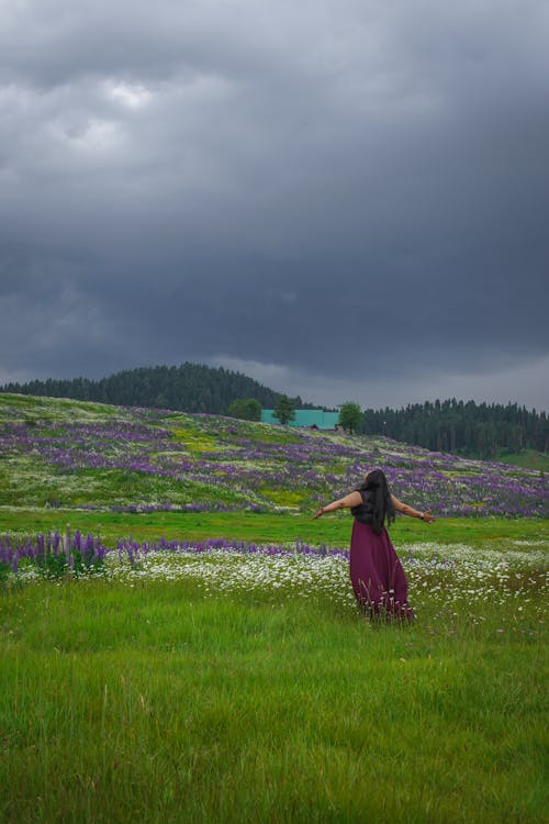 A Woman Standing on the Green Grassland Under Gray Clouds