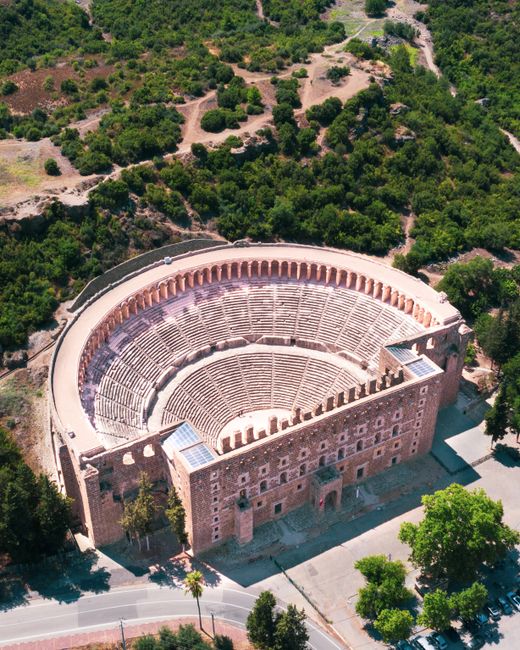 Drone shot of the Aspendos Theater, a historical landmark in Turkey, surrounded by lush greenery.