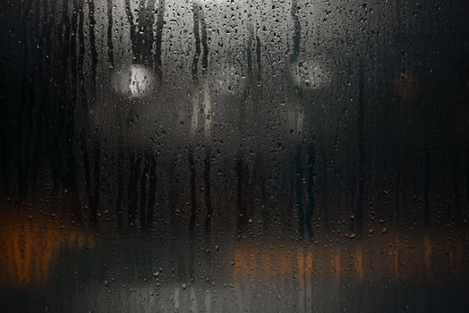 Rain-soaked window with droplets and reflections at night, creating a moody urban ambiance.