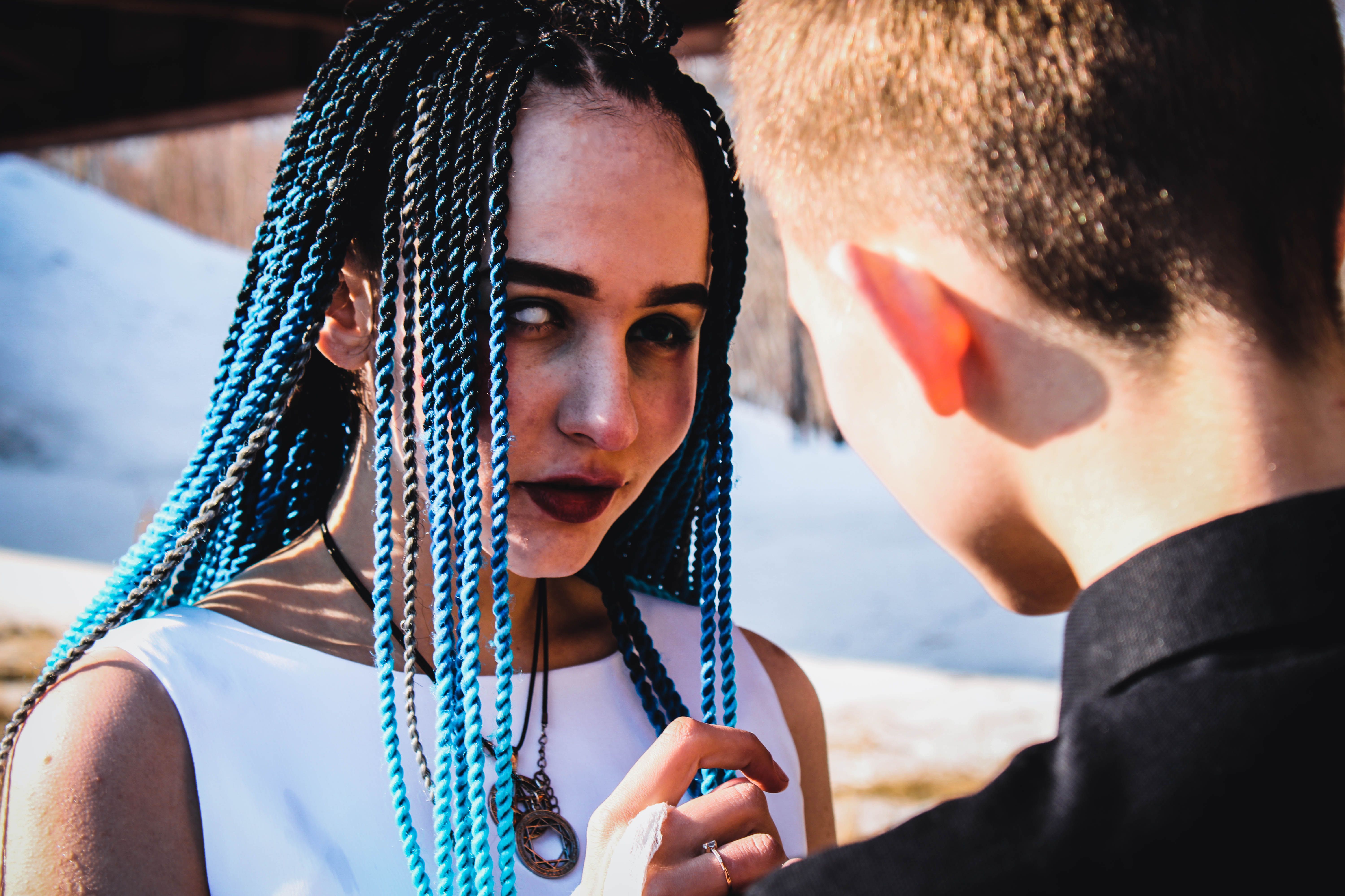 Young couple interacting outdoors. Woman with vibrant blue braided hair wearing necklaces.