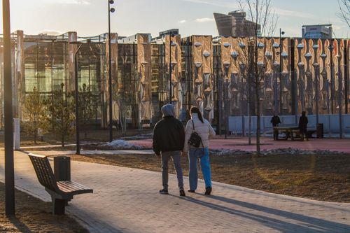 Free A couple walks in a modern urban park during sunset with contemporary architecture in the background. Stock Photo