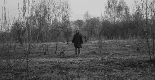 Grayscale Photo of a Man in Black Coat Standing on a Grassy Field
