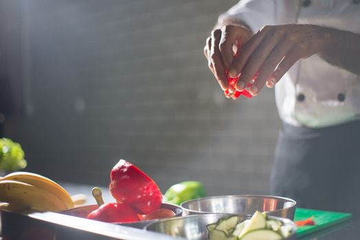 A chef skillfully slices red peppers and other vegetables in a well-lit kitchen.