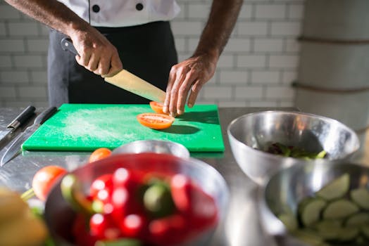 Chef skillfully slicing tomatoes on a chopping board in a commercial kitchen, highlighting culinary preparation.