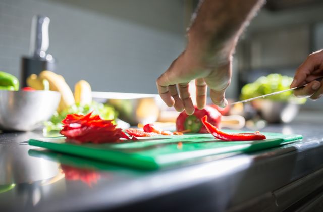 Hands slicing a red pepper on a chopping board in a home kitchen