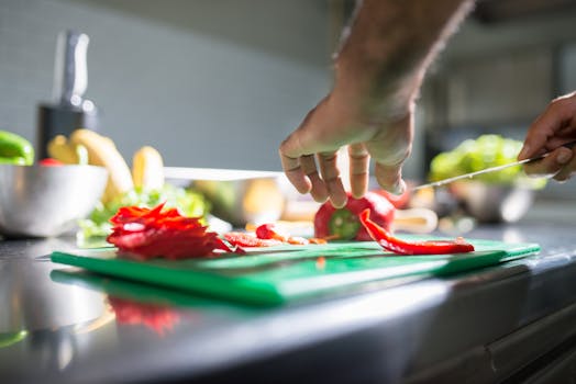 Hands slicing red bell pepper on a chopping board in a kitchen setting, ideal for culinary visuals.