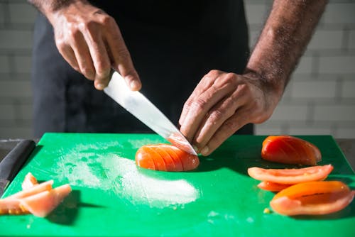 Person Slicing Tomato on Green Chopping Board