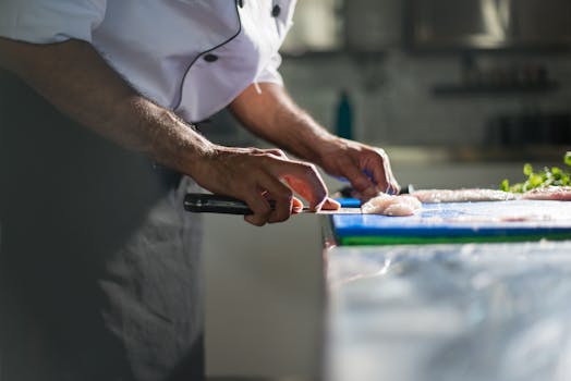 Close-up of a chef expertly slicing fish fillet in a professional kitchen setting.