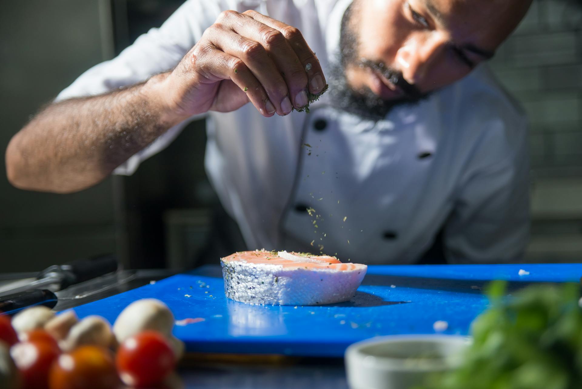 A Chef Sprinkling Herb on Top of Sliced Fish