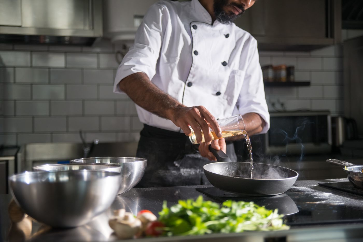 Chef pouring oil into a frying pan in a professional kitchen
