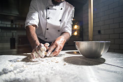 A Person in White Chef Uniform Kneading a Dough