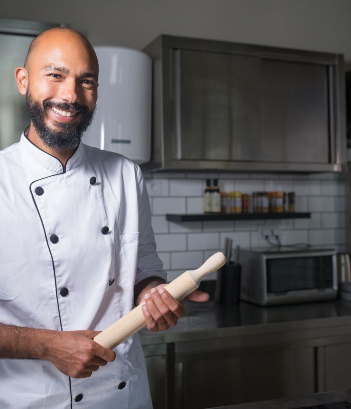 Smiling chef in white chef's jacket holding a rolling pin in a professional kitchen