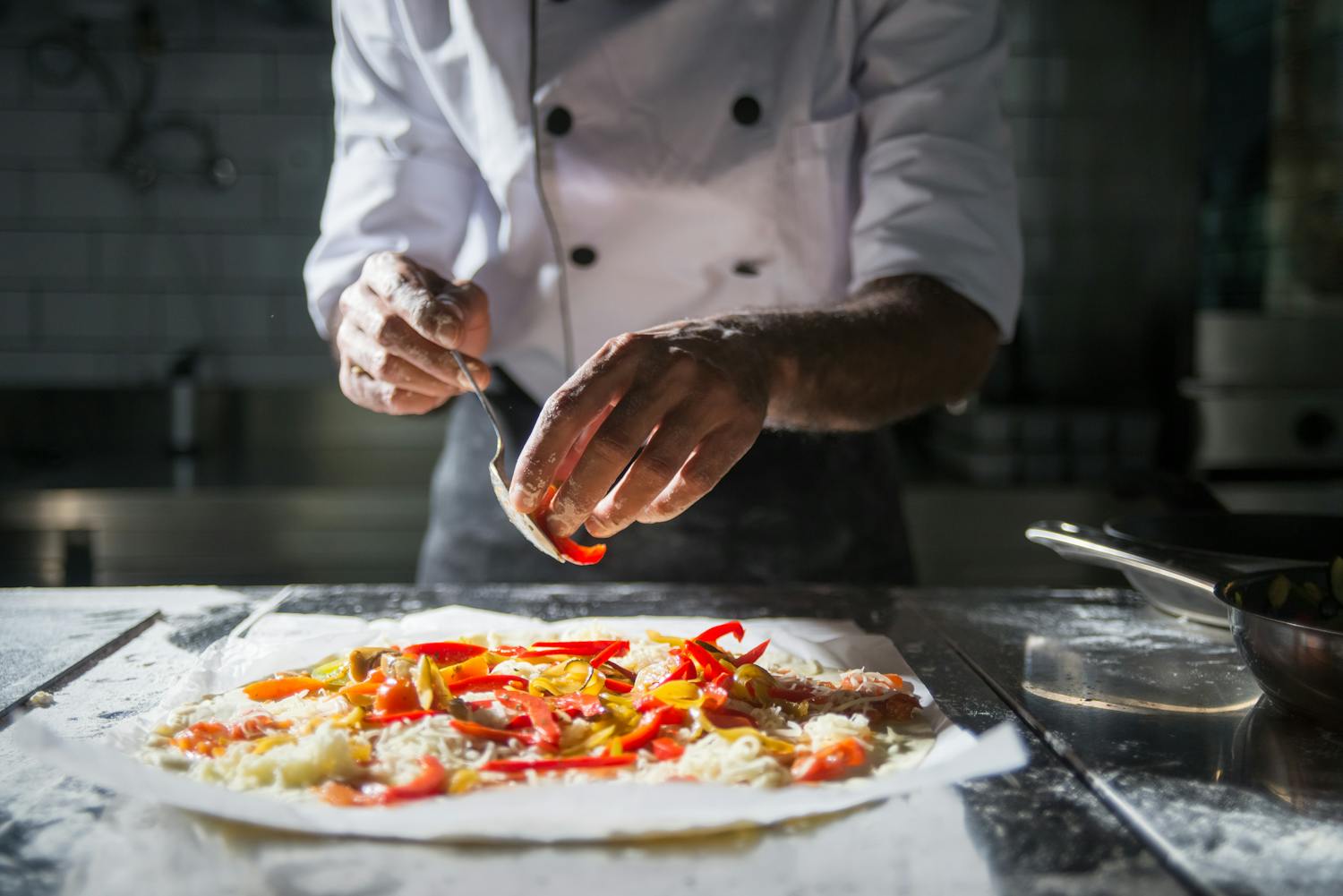 Close-up of a chef adding fresh toppings to a pizza dough in a professional kitchen.