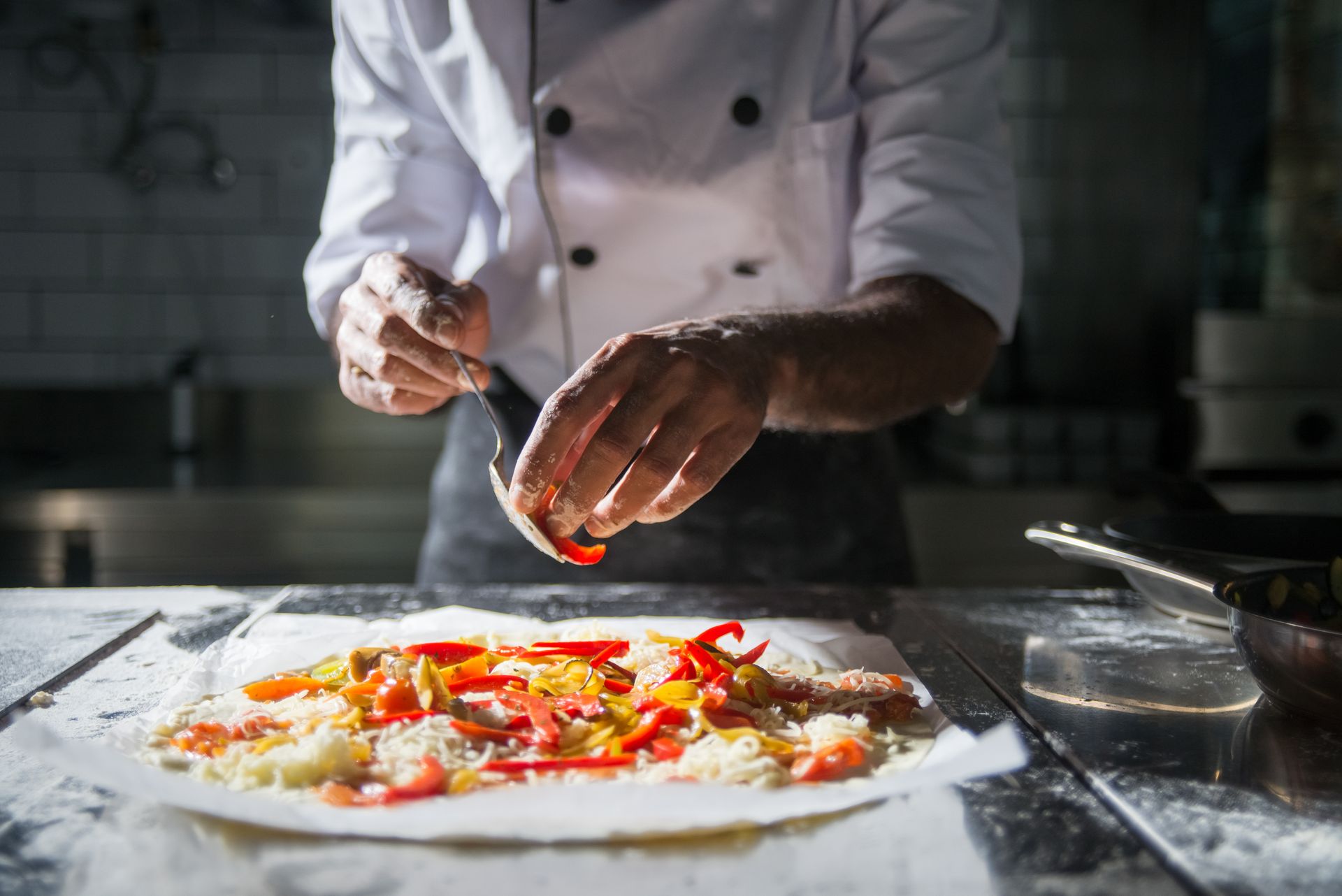 A Person Wearing Chef's Uniform Putting Ingredients on the Dough