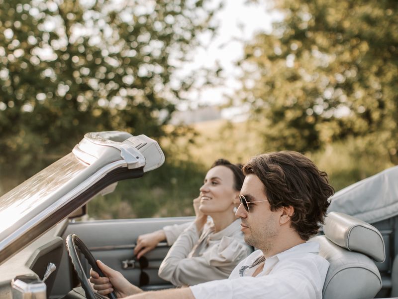 Happy couple driving a convertible through the countryside on a sunny day - history driving tours
