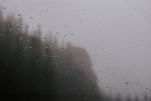 Raindrops on a window create a moody, atmospheric view of a misty landscape.