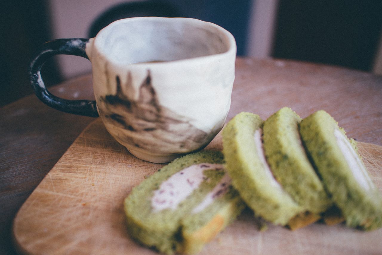 sliced matcha roll cake on wooden board with ceramic tea cup warm invi