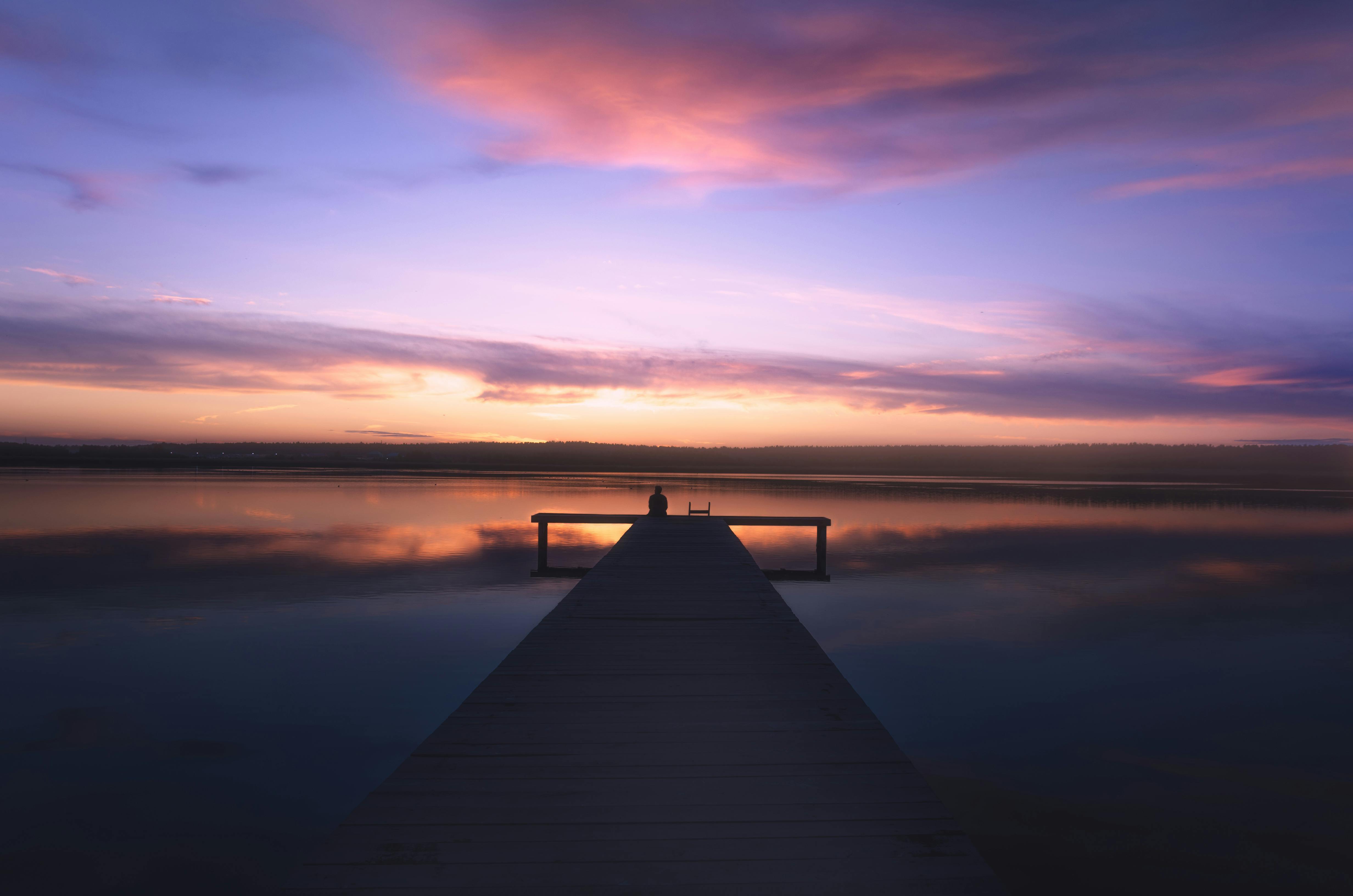 Peaceful scene of a sunset over a wooden dock on a calm lake, reflecting vibrant colors.
