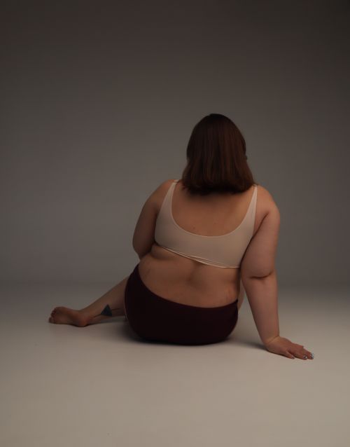 Free Back view of a plus size woman sitting in a studio, embracing body positivity and comfort. Stock Photo
