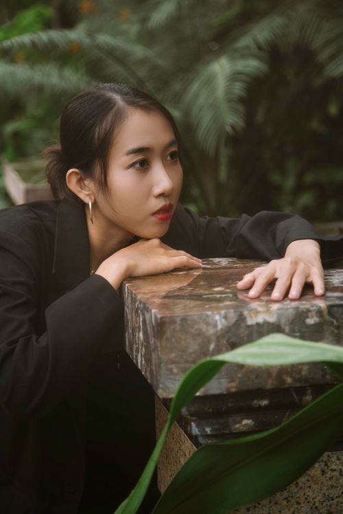 Free Close-up portrait of a woman in a lush garden, resting on a stone surface with a thoughtful expression. Stock Photo