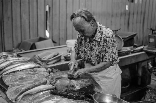 Grayscale Photo of an Elderly Woman Cleaning a Fish