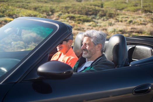 Happy senior couple driving a luxury convertible car on a sunny day outdoors in Portugal.