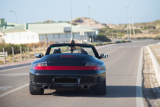 A sleek black convertible cruising down a scenic coastal road under clear skies.