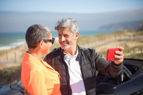 Free A senior couple enjoying a sunny day at the beach while taking a selfie with a smartphone. Stock Photo