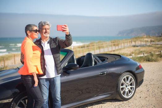 Elderly couple enjoys a scenic seaside drive in Portugal, capturing memories with a selfie.
