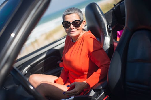 Senior woman in orange dress sitting in a convertible car by the seaside in Portugal.