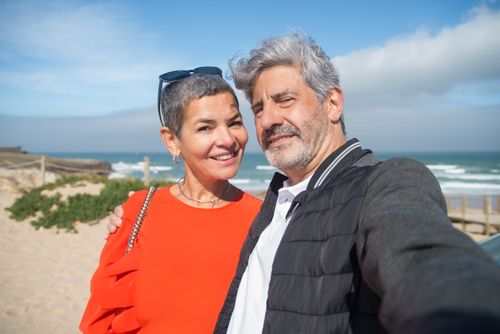 Free Smiling couple taking a selfie on a sunny beach in Portugal, capturing a joyful moment. Stock Photo