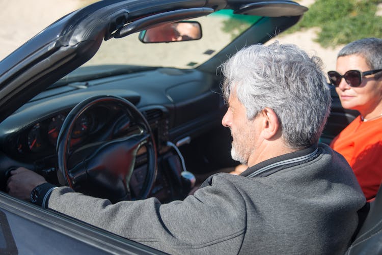 A Man Driving A Convertible Car With A Woman Wearing Sunglasses