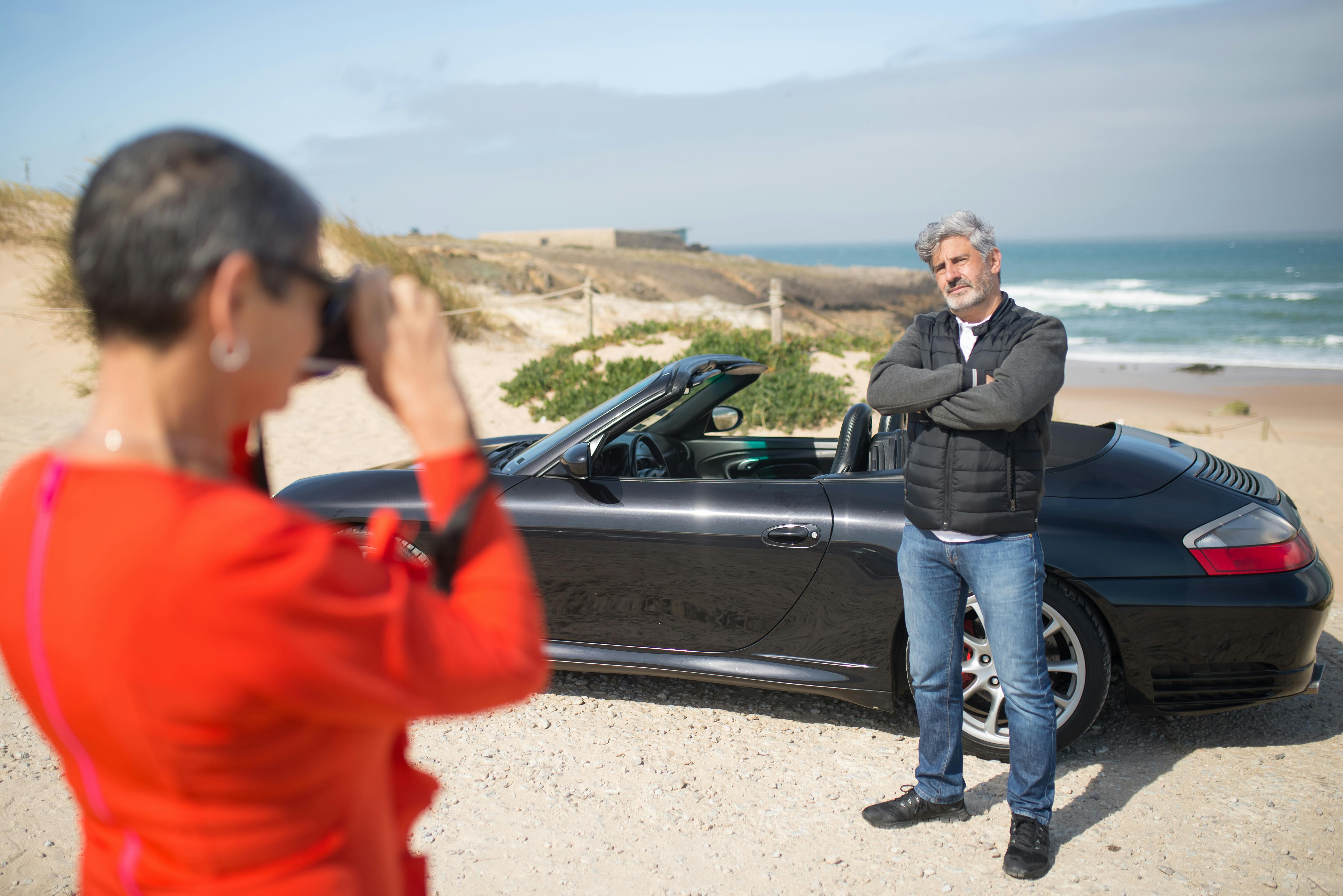 Couple enjoying a beach road trip in Portugal, posing with a convertible car, capturing joyful travel moments.