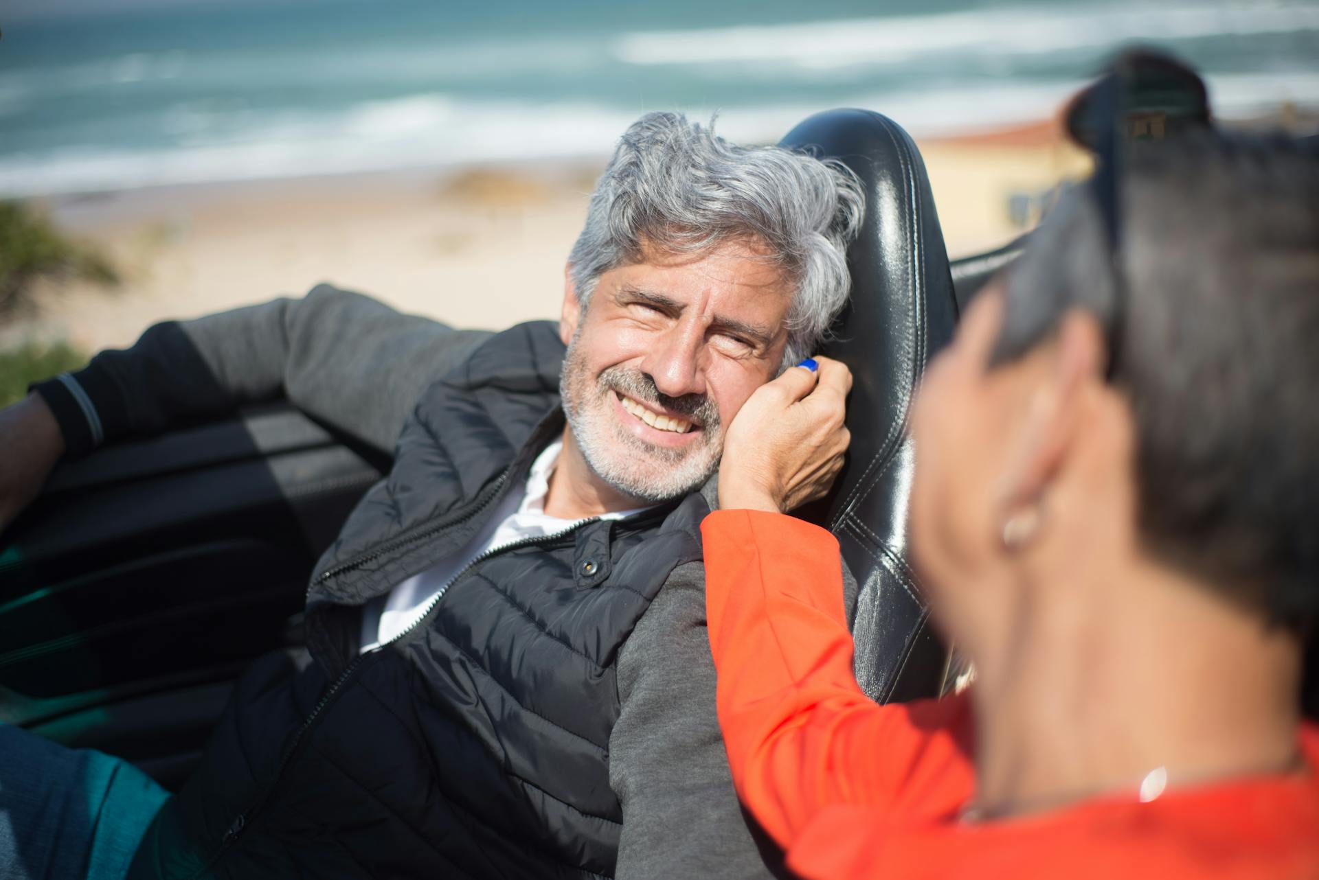 Senior couple smiling and enjoying a drive in a convertible by the beach in Portugal.