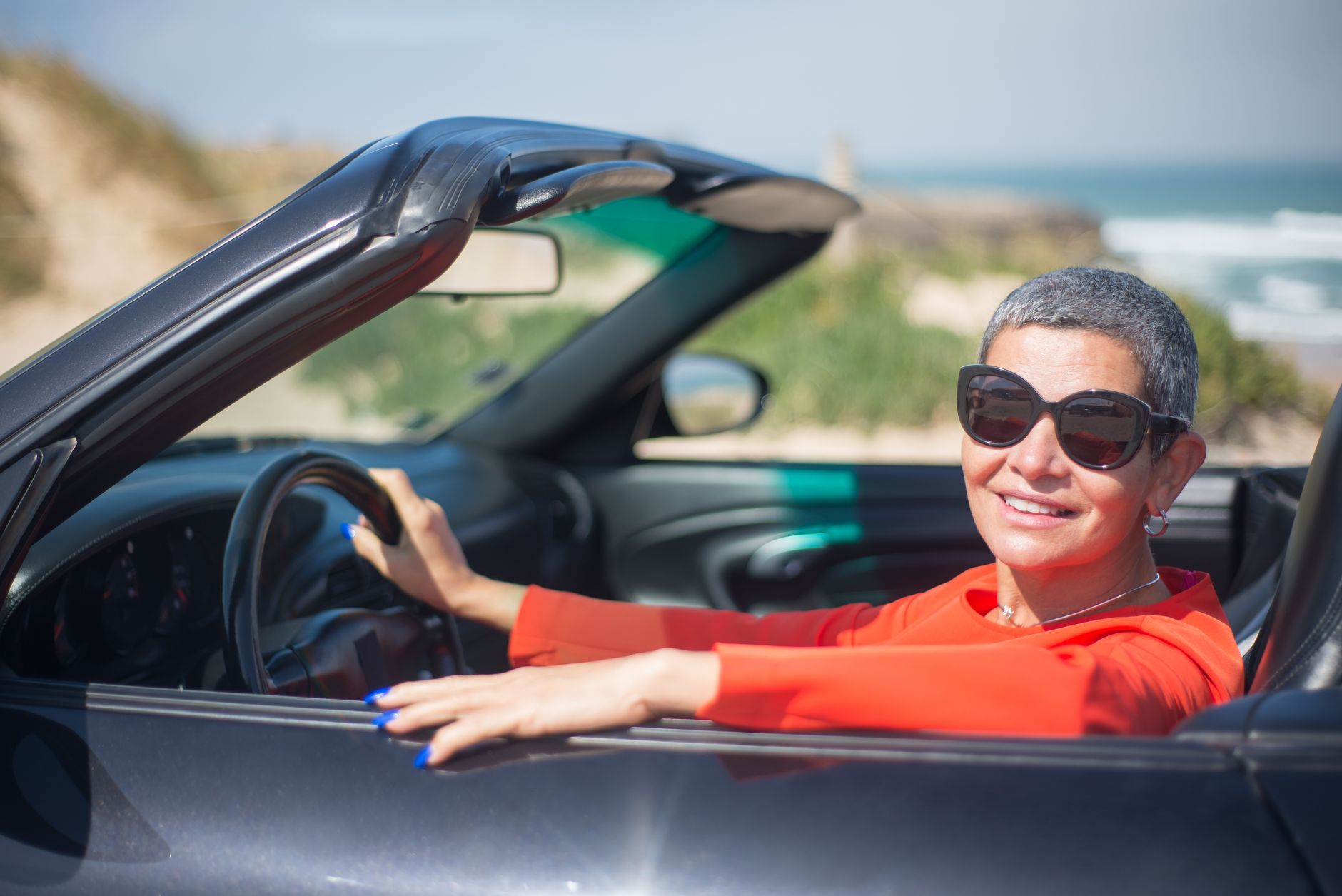 A cheerful woman enjoying a sunny drive in a convertible by the seaside.