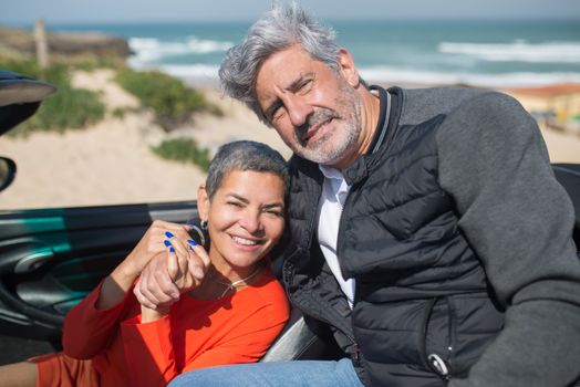 Smiling senior couple embracing during a sunny beachside road trip in Portugal.