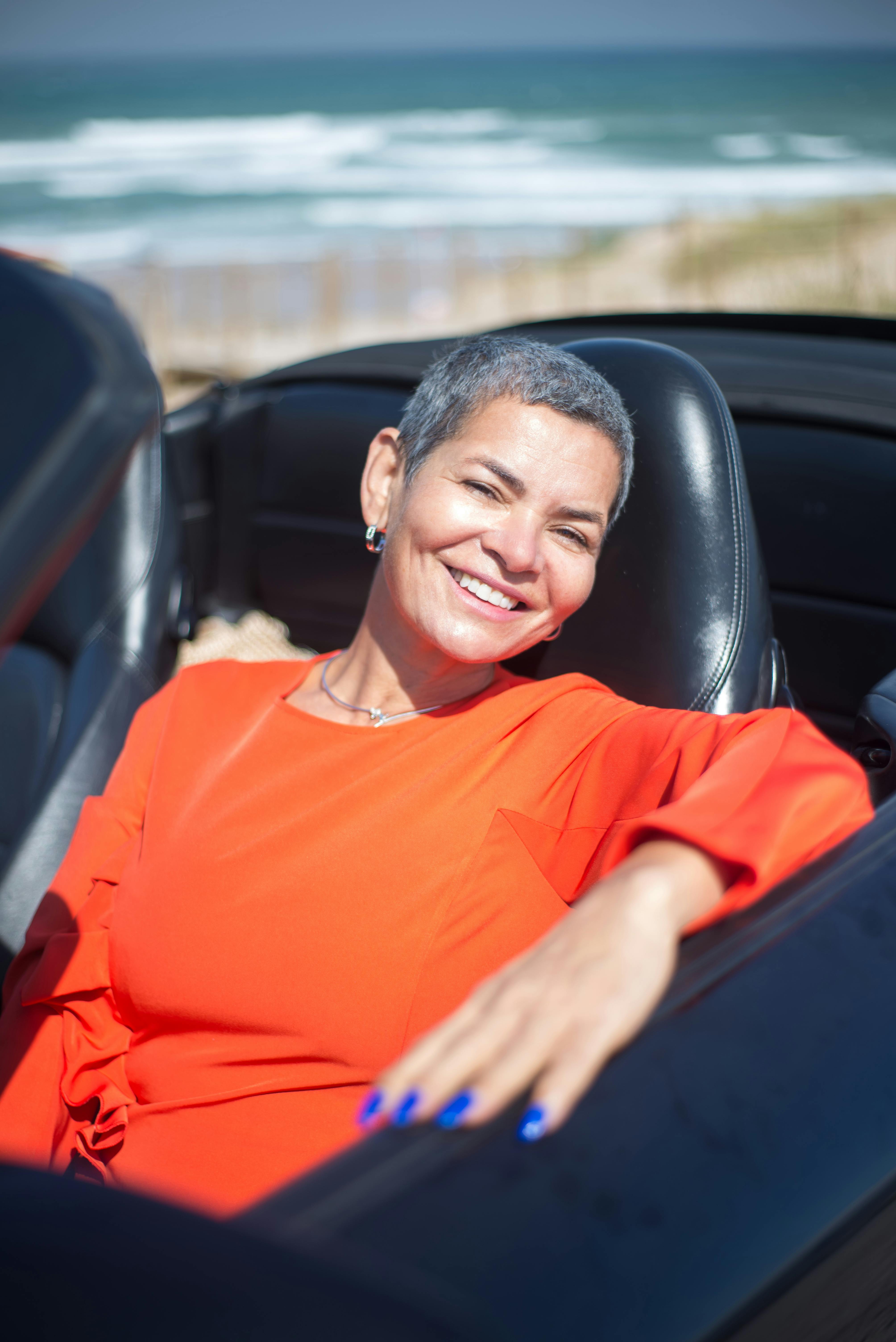 Smiling woman in a black convertible by the beach on a sunny day in Portugal.