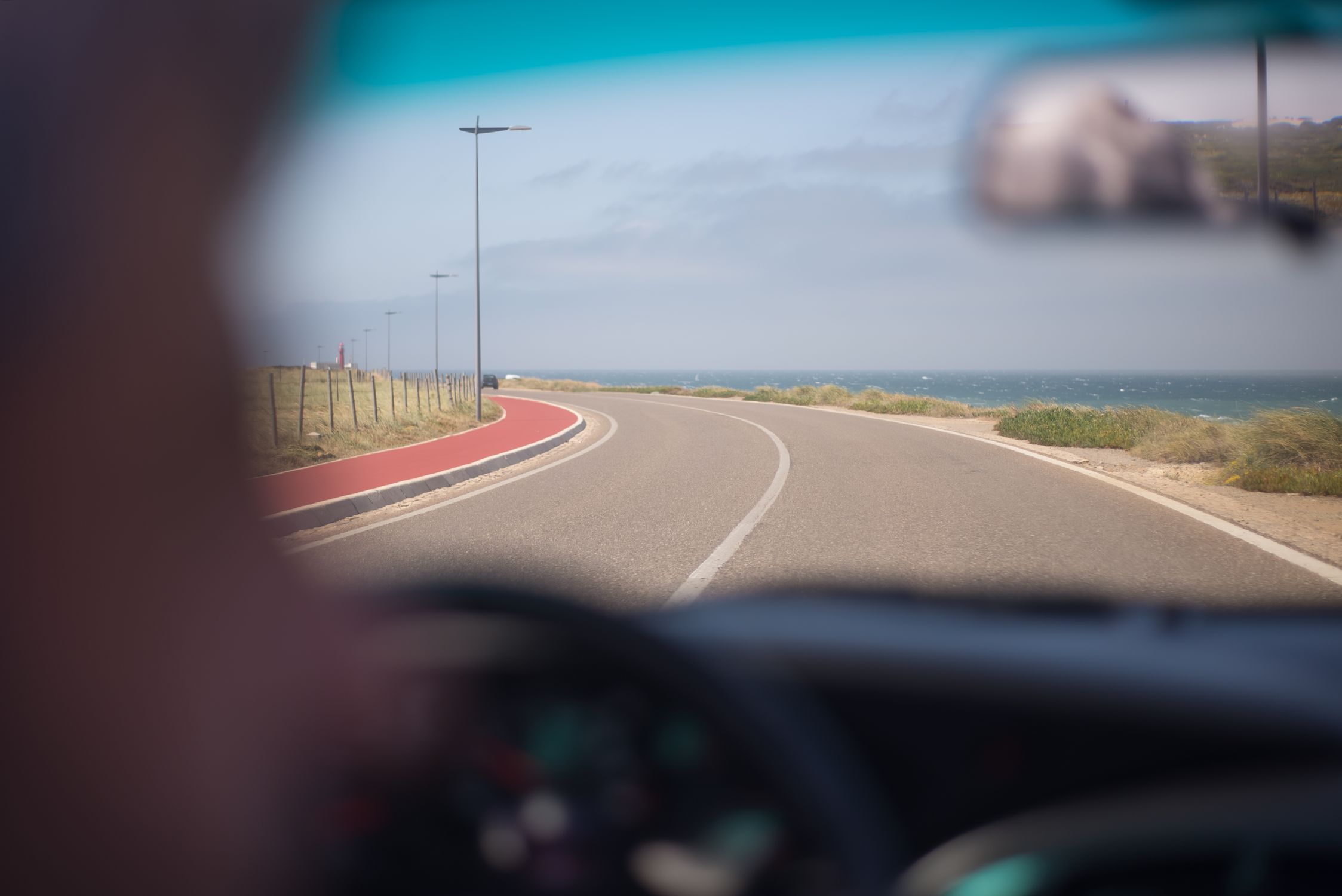 A scenic drive along the Portuguese coastline on a sunny day, viewed through a windshield.