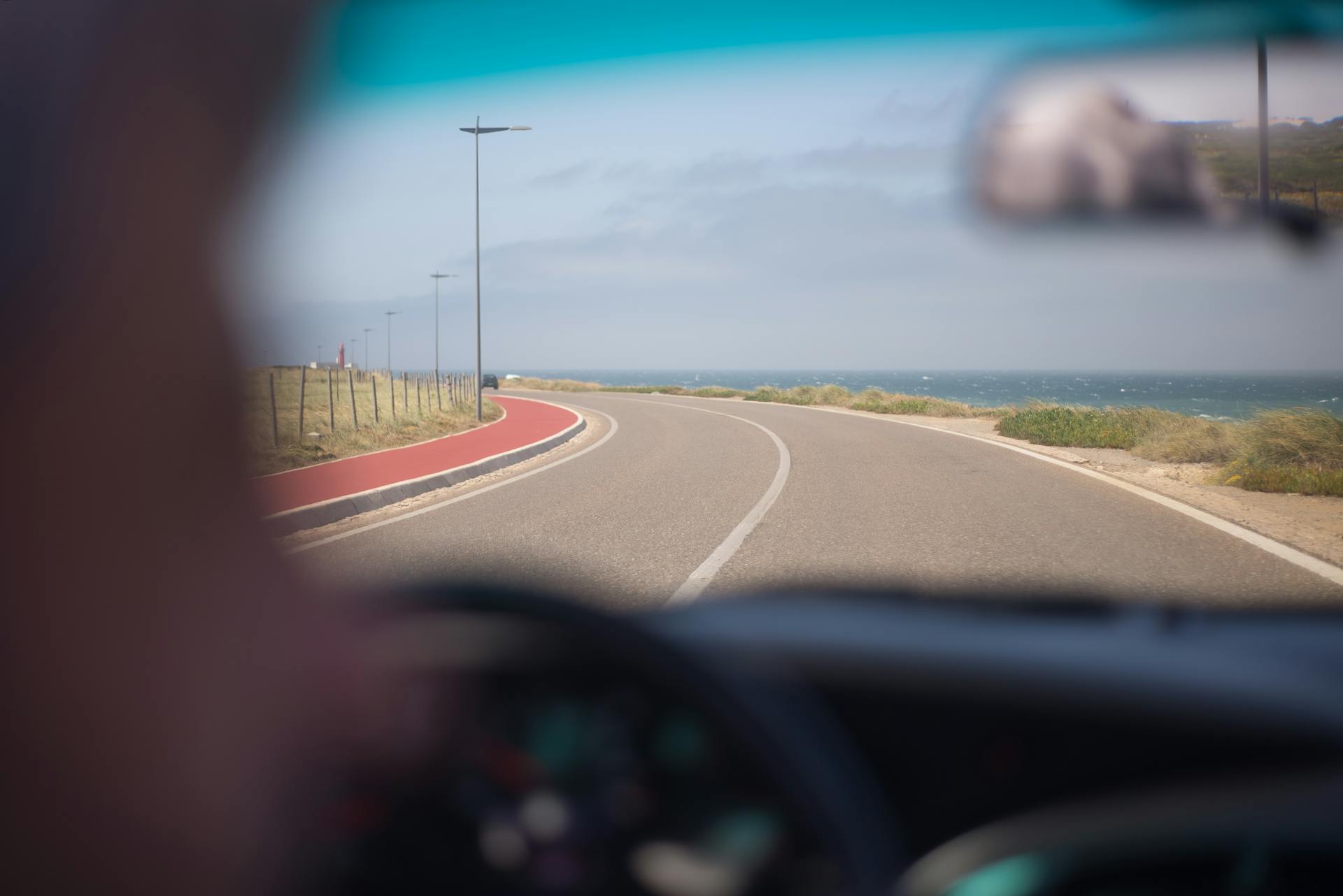 A scenic drive along the Portuguese coastline on a sunny day, viewed through a windshield.