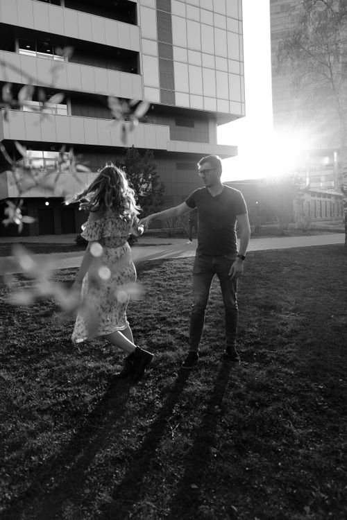 Free A couple joyfully dances in an urban park setting as the sun sets, captured in grayscale. Stock Photo