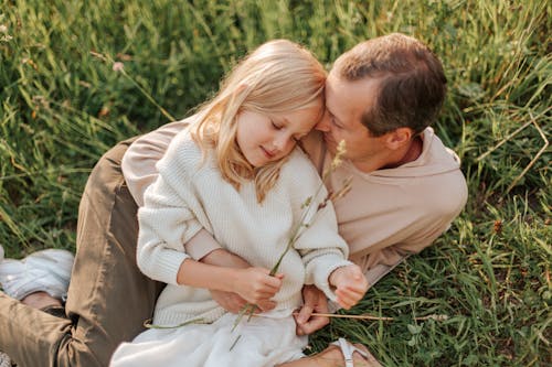 Father and Daughter Sitting on the Grass Field