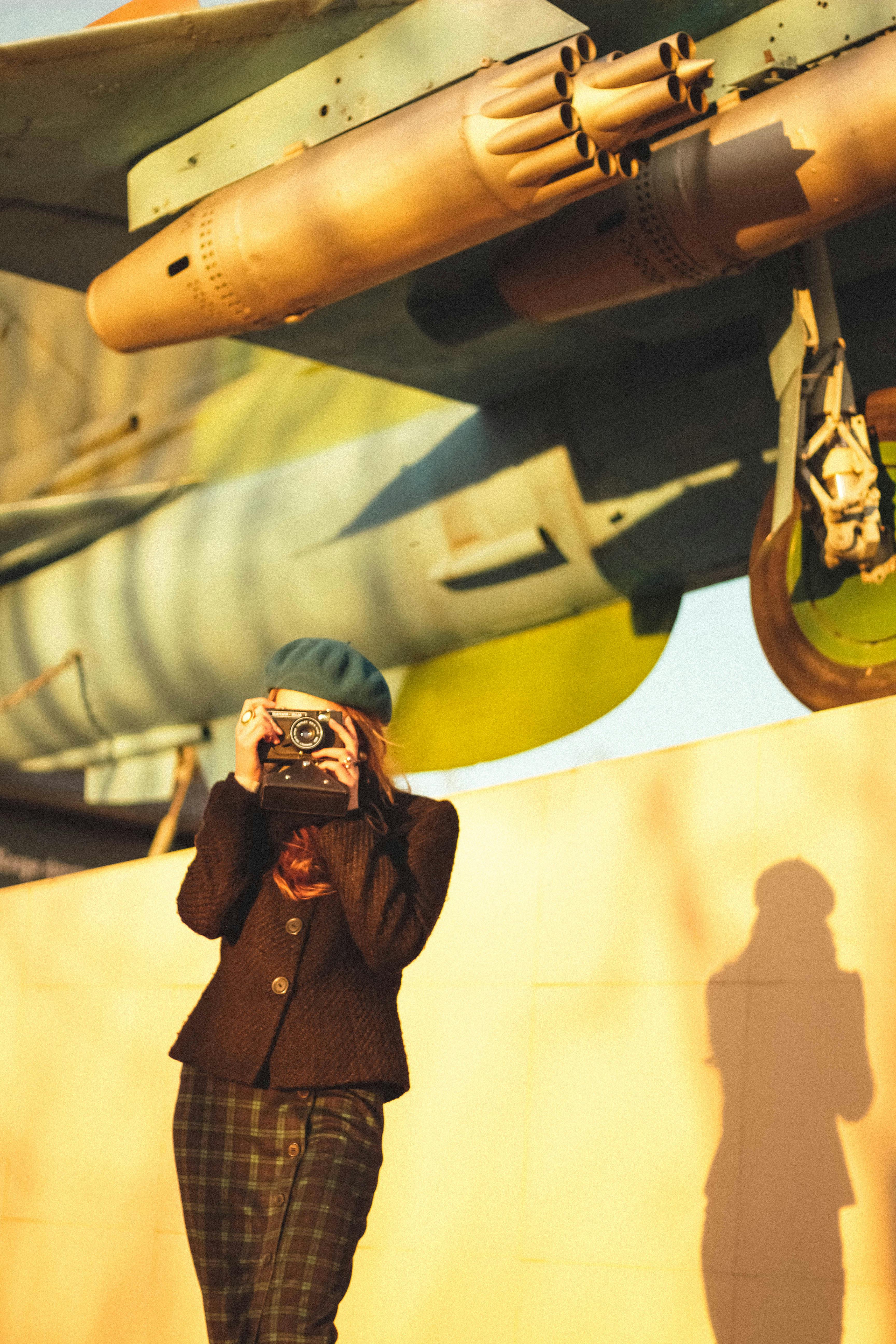 Woman with vintage film camera under a retro aircraft in warm light.