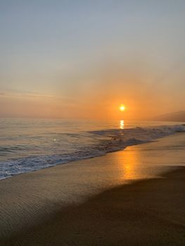 Tranquil sunset on a sandy beach with gentle waves lapping at the shore.