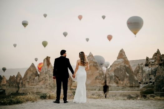 Back View of Groom and Bride with Tuff Rock Formations and Hot Air Balloons in Sky