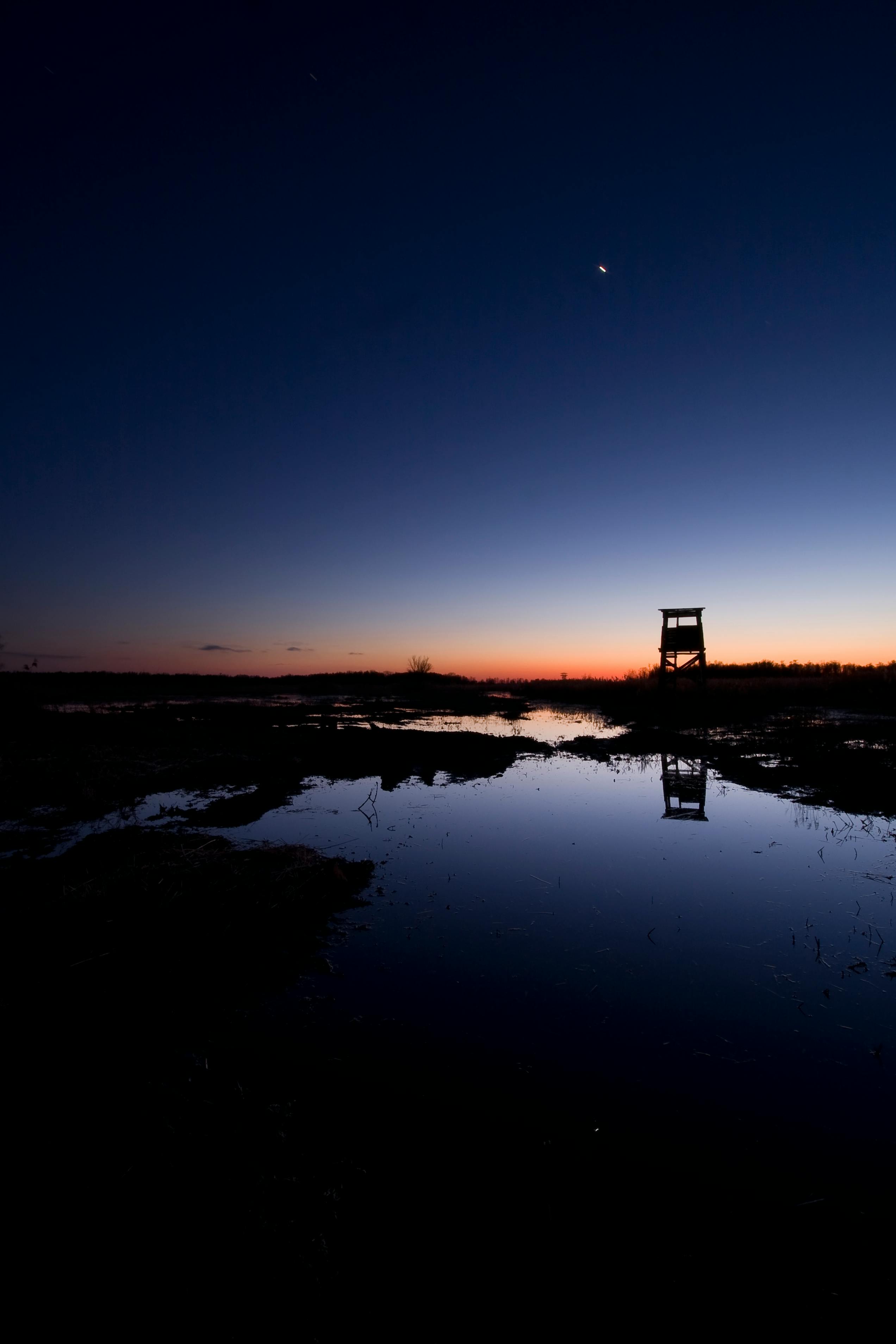 Stunning twilight landscape with lake reflection and silhouette observation tower.