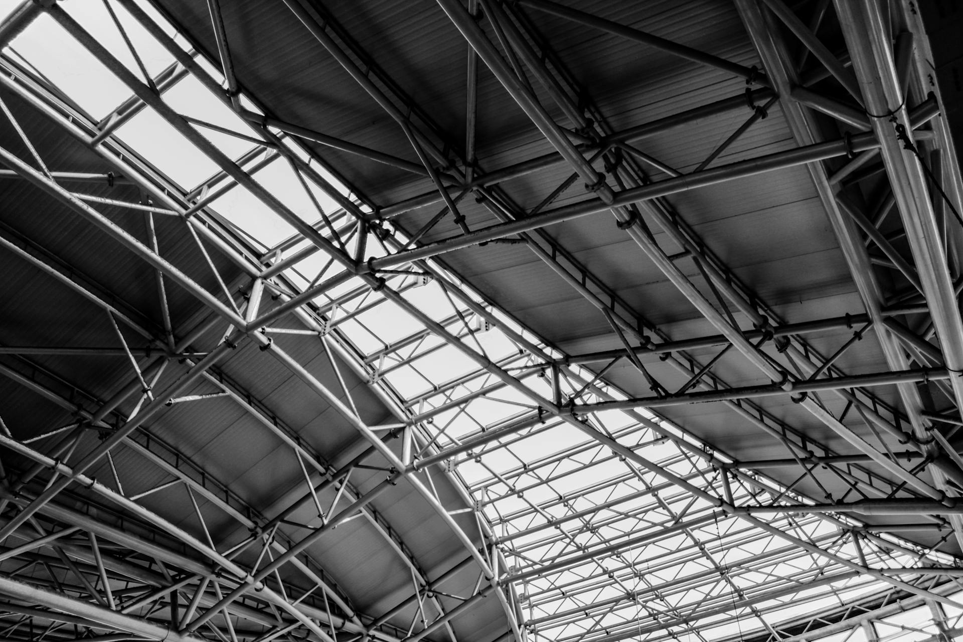 Black and white photo of geometric steel truss ceiling structure, highlighting industrial architecture.