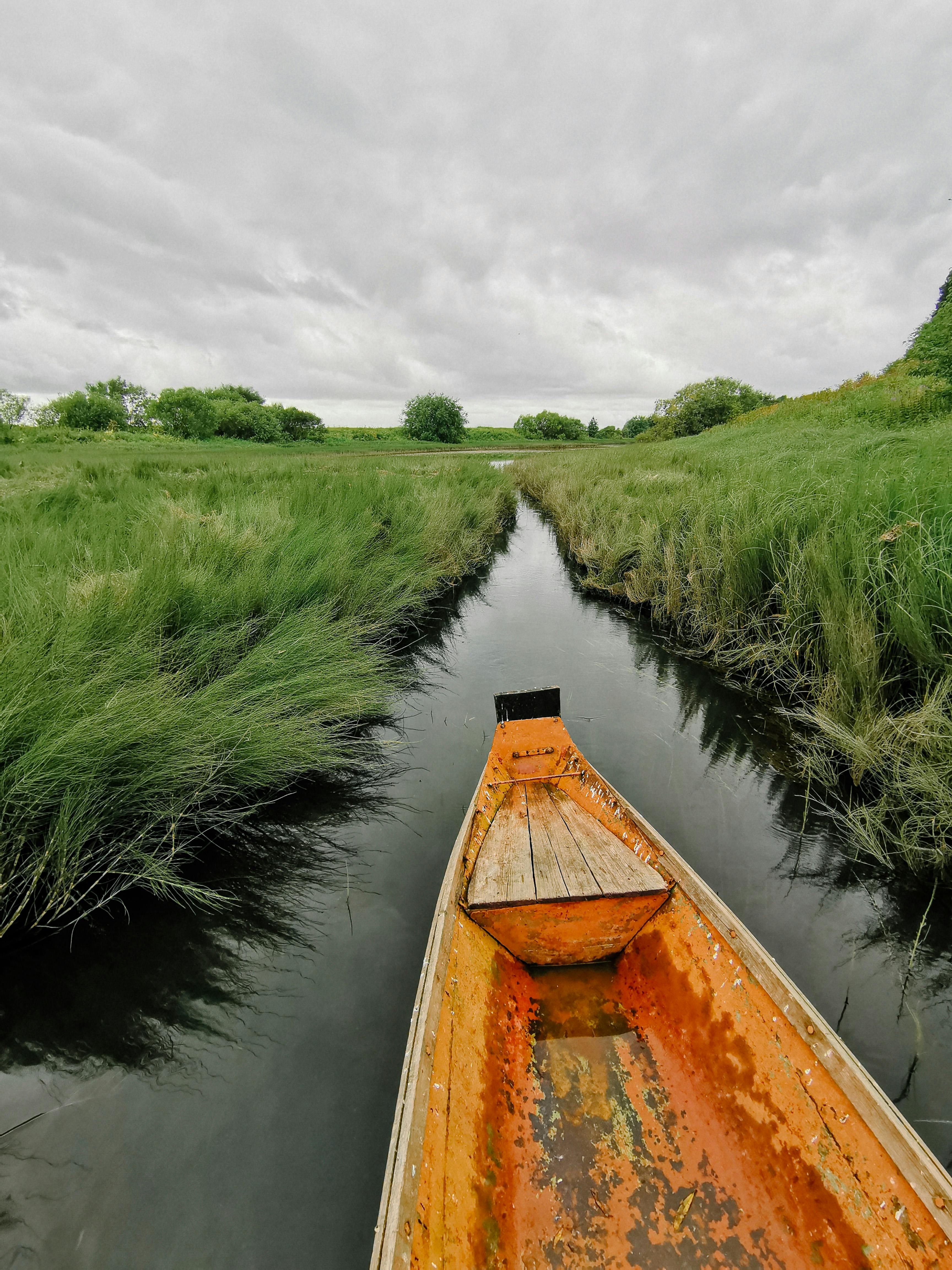 Free Explore the serene landscapes of Karpogory, Russia, with a rustic boat on a grassy canal under a cloudy sky. Stock Photo
