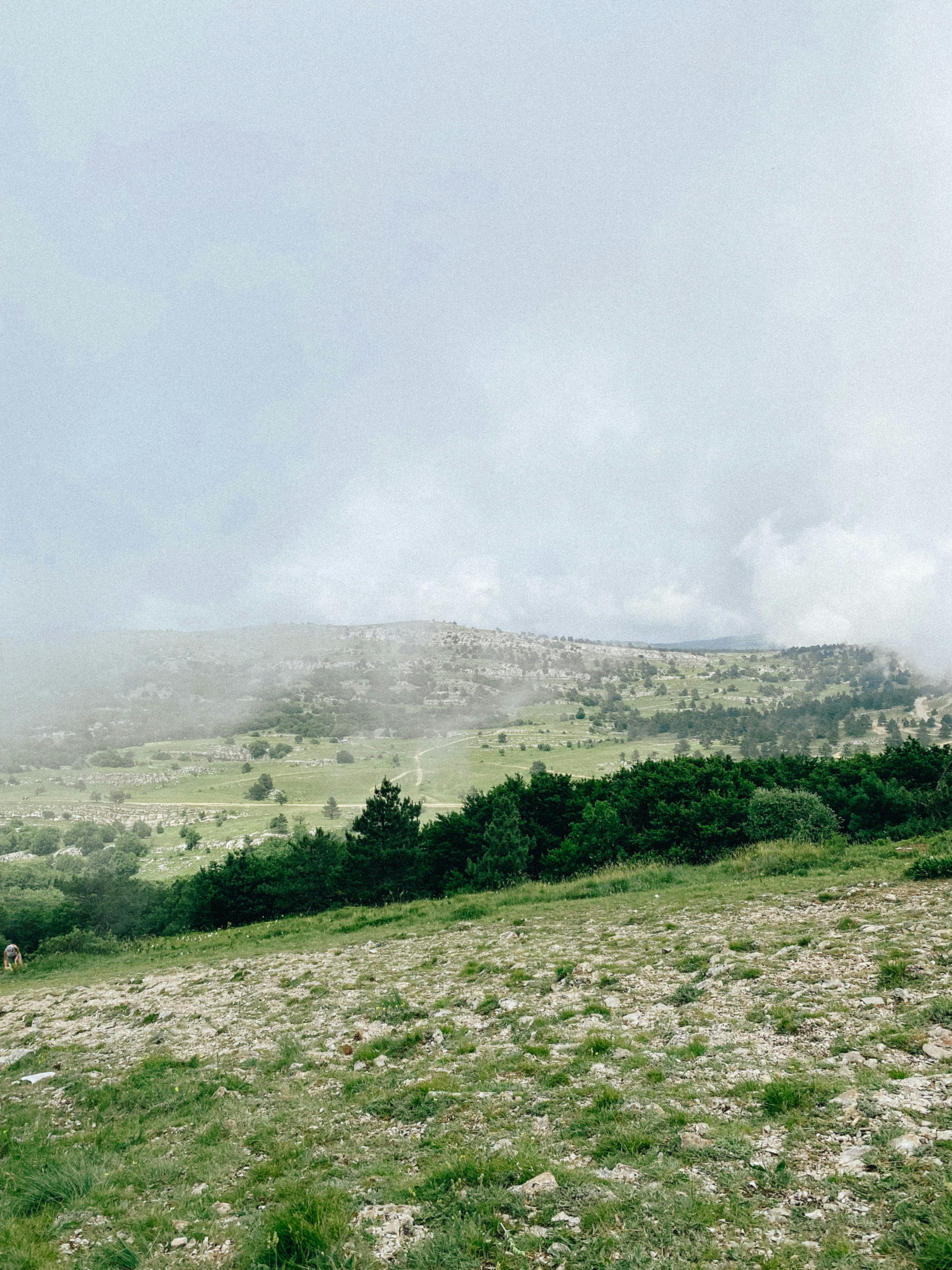 Serene misty mountain landscape with green fields and cloudy sky, a perfect nature scene.