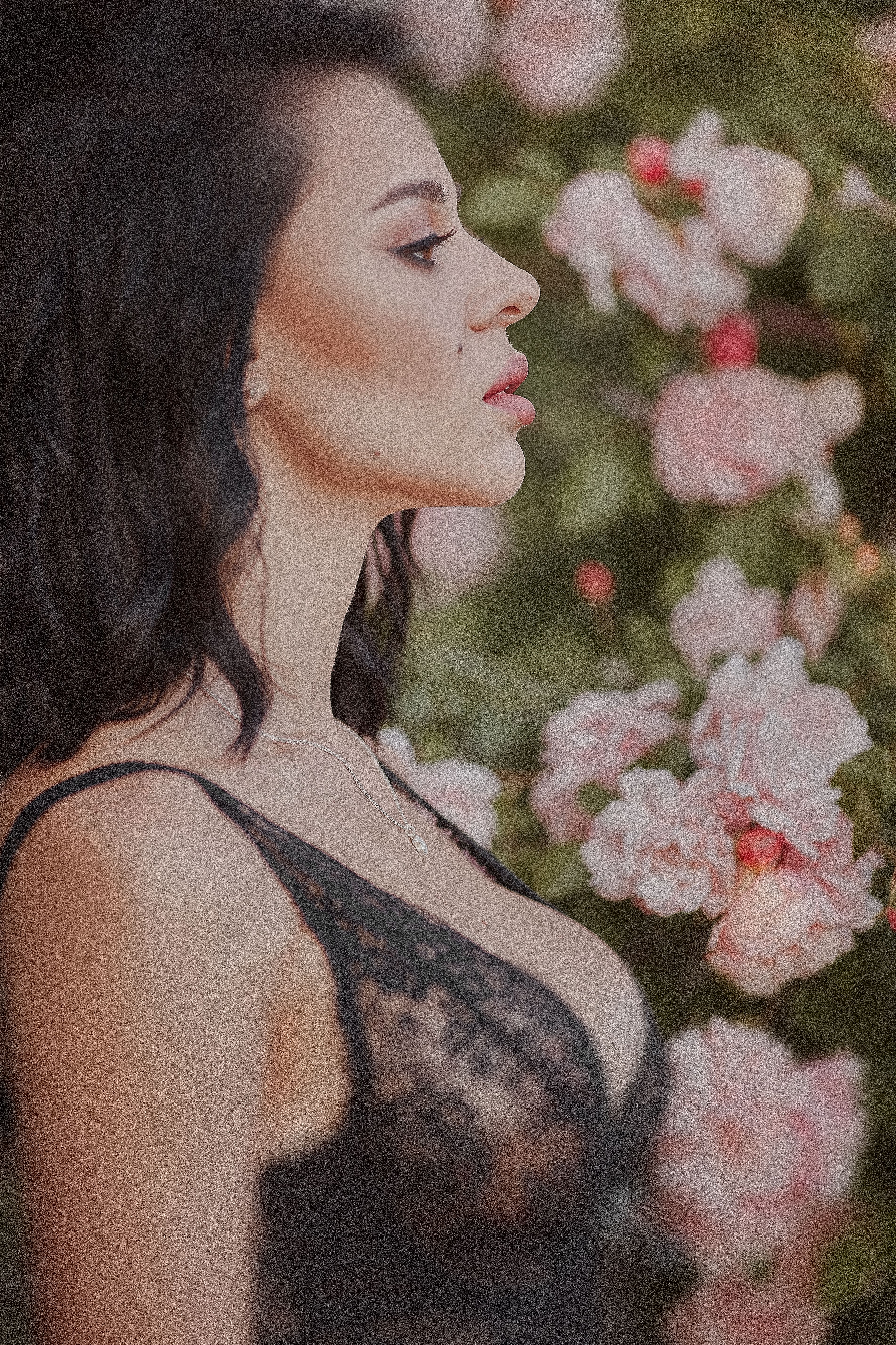 Elegant side profile portrait of a woman in a black lace top against a lush floral background.